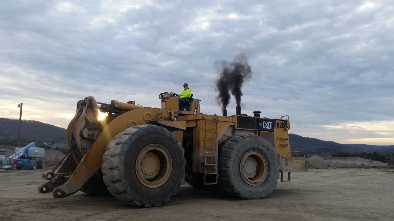 Yellow CAT 992C wheel loader emitting thick black smoke from dual exhaust stacks at dusk.