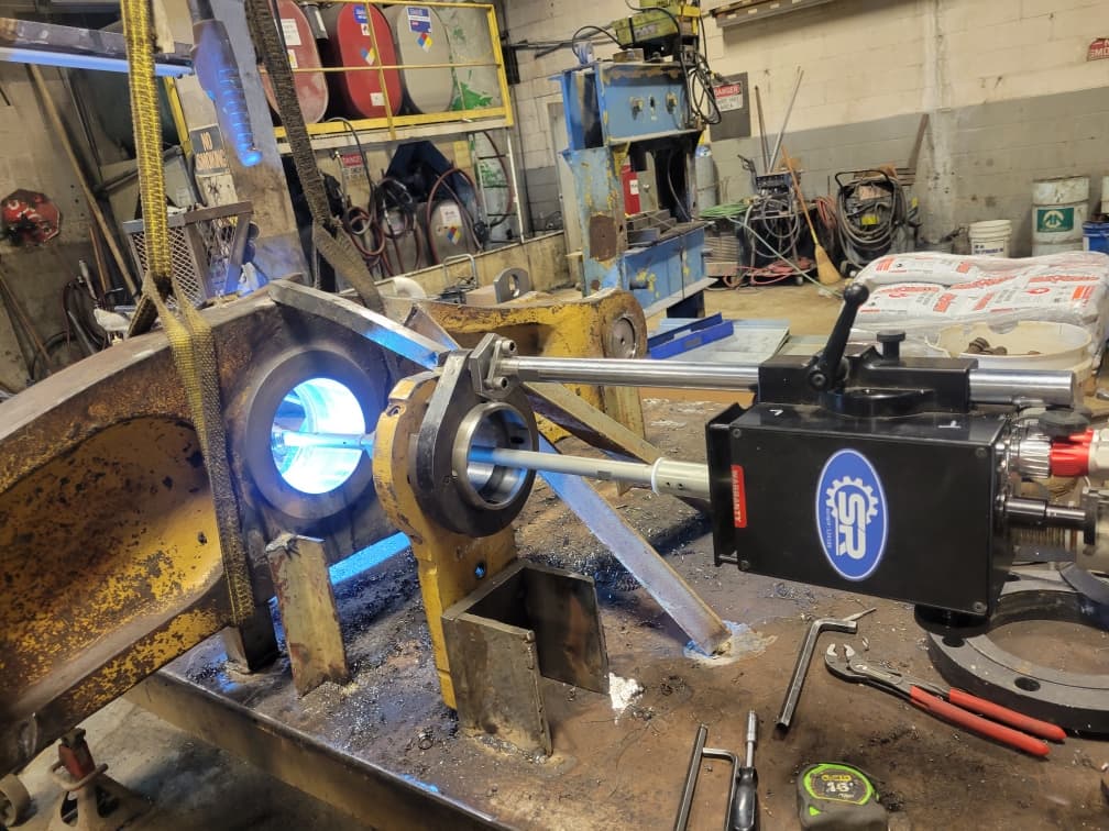 Portable SR machine with bright blue light boring into a large yellow industrial metal component.