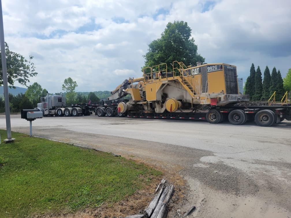 Large yellow Caterpillar 992G loader transported on a multi-axle semi-trailer along a road.