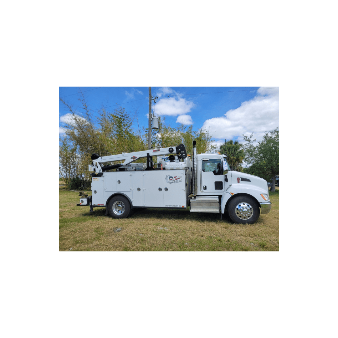 White Kenworth service truck with a crane and storage compartments parked on a grassy field.
